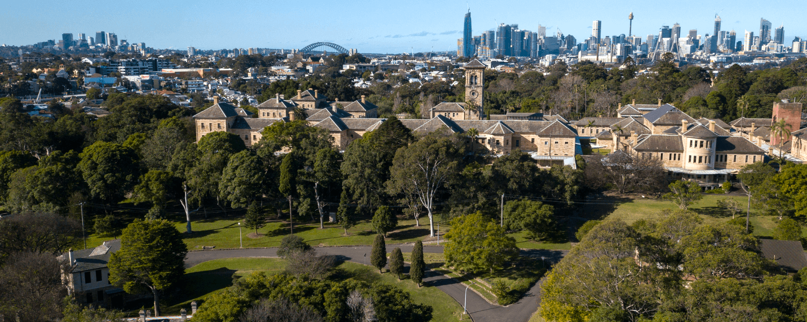 An aerial view over Callan Park with the Kirkbride building in the foreground, and Sydney city skyline in the background.
