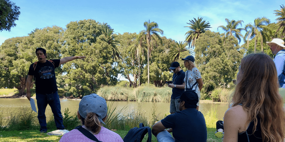 A tour guide presents to a crowd of people by a pond in Centennial Park.