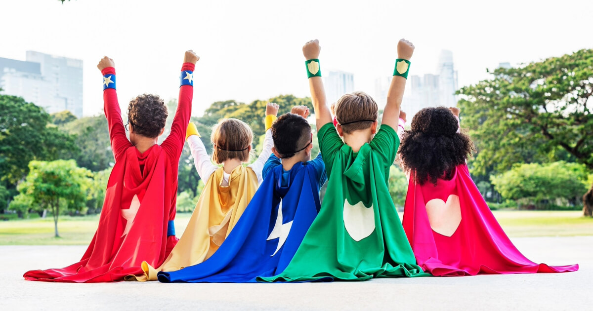 A group of children dressed as superheroes with colourful capes and raised fists, facing a scenic park view with a city skyline in the background, symbolising teamwork and empowerment.