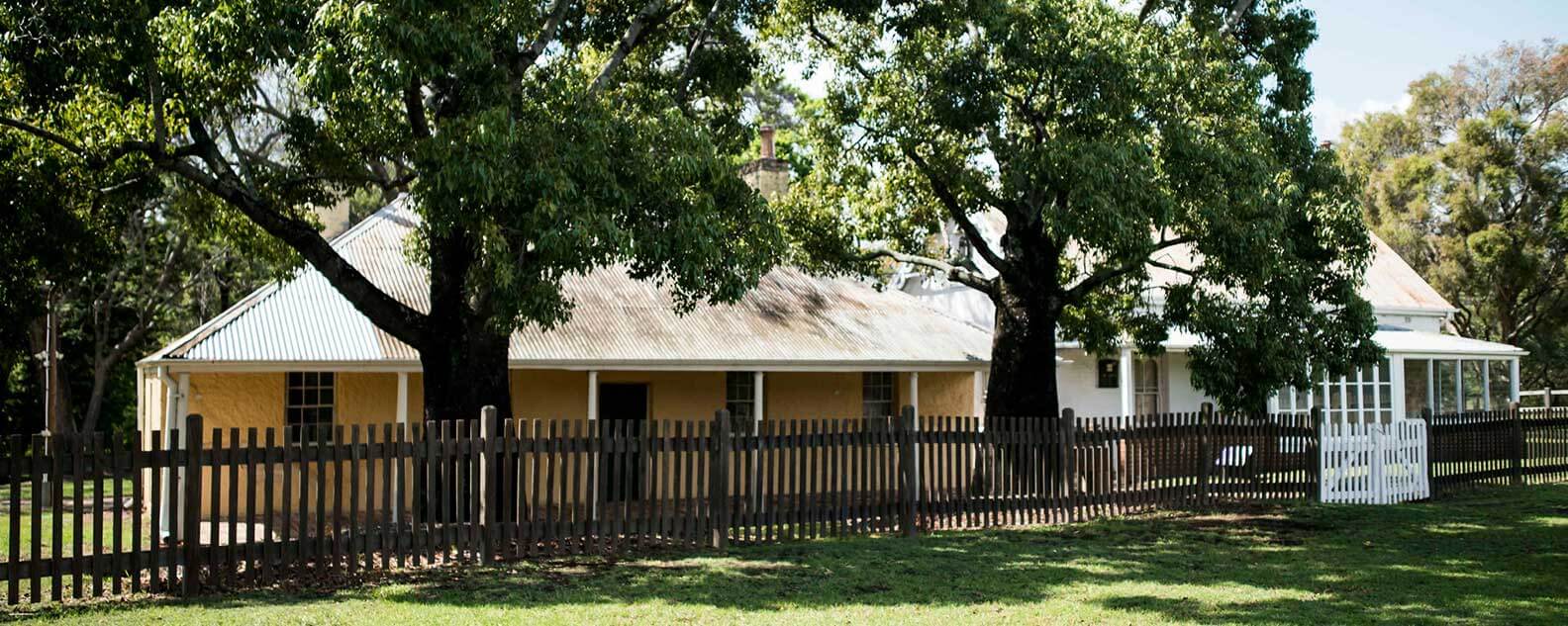 A cottage surrounded by a fence and tall trees in the yard, creating a cozy and inviting atmosphere.