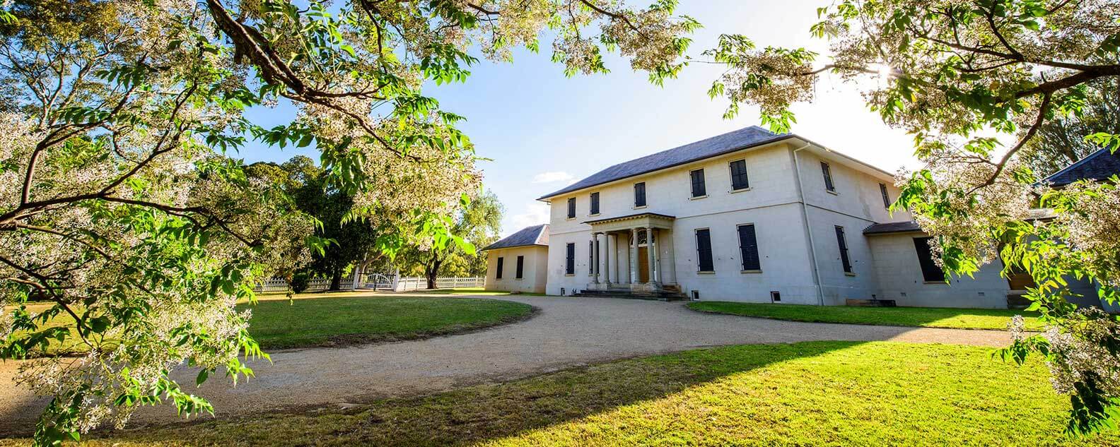 A historic government house surrounded by vibrant trees and grassy areas, showcasing its charming and tranquil setting.