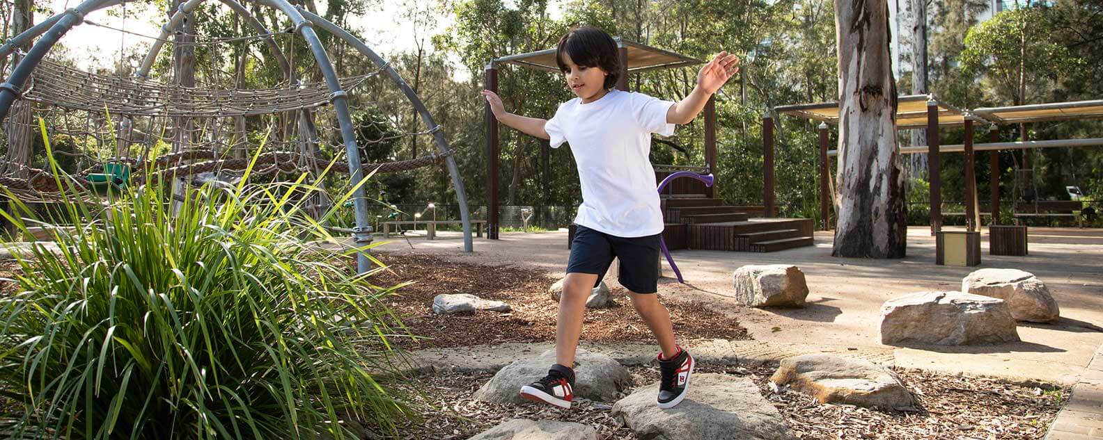 A young boy joyfully jumps from rock to rock in a colorful playground, enjoying a sunny day of fun and adventure.