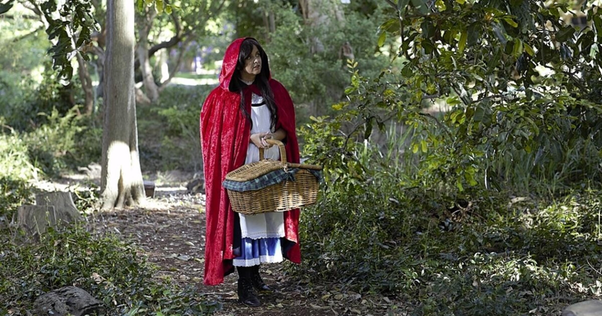 A women dressed up in a red coat carrying a basket, depicting Little Red Riding Hood.  