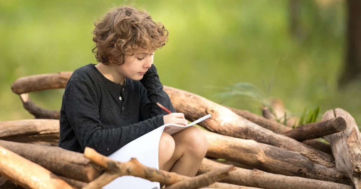 Young boy sitting on some logs working through a workbook