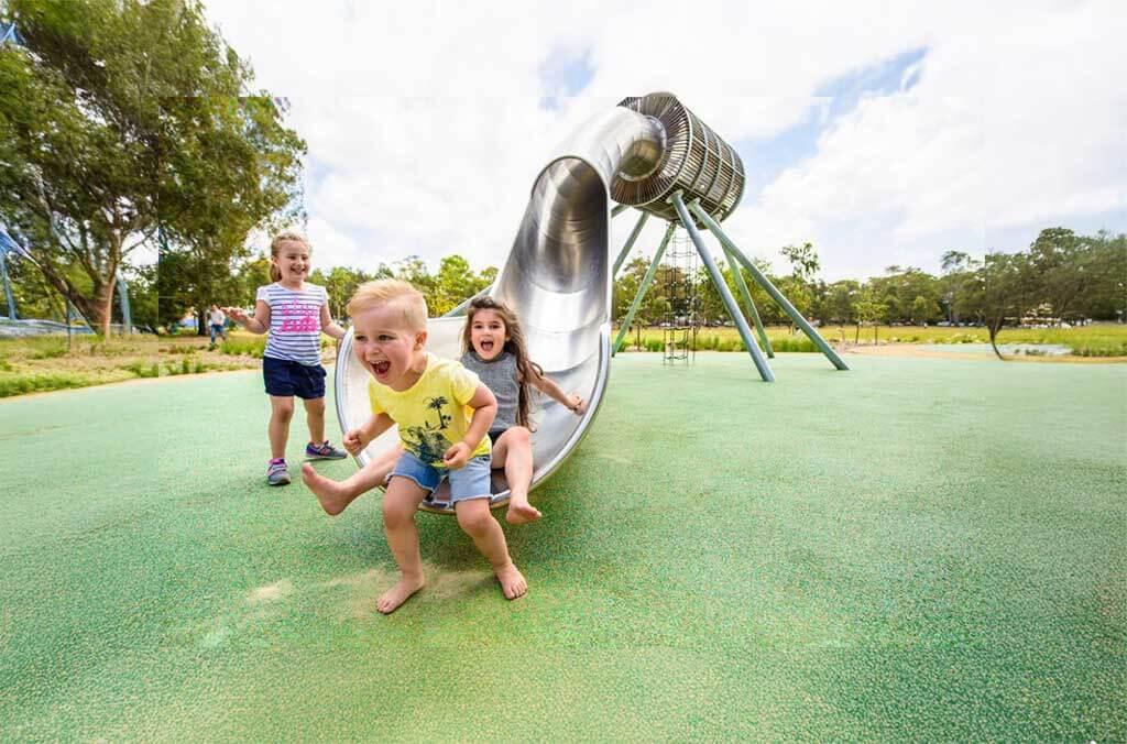 Kids playing on a slide at Domain Creek Playground, smiling and having fun on a beautiful day outdoors.