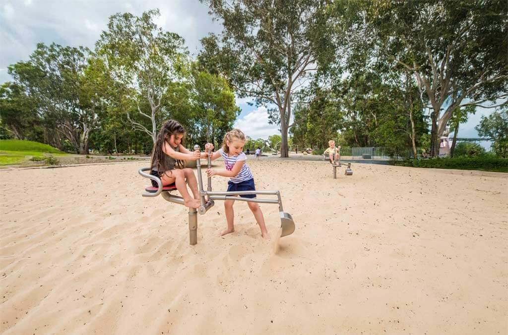 Two children having fun in the sand at Domain Creek Playground, laughing and playing in the warm sunshine.