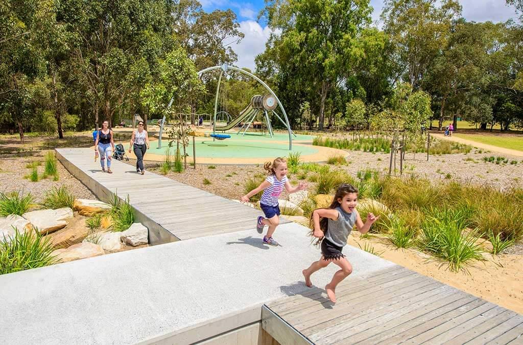 Two children running on a wooden walkway at Domain Creek Playground, filled with laughter and fun in the park.