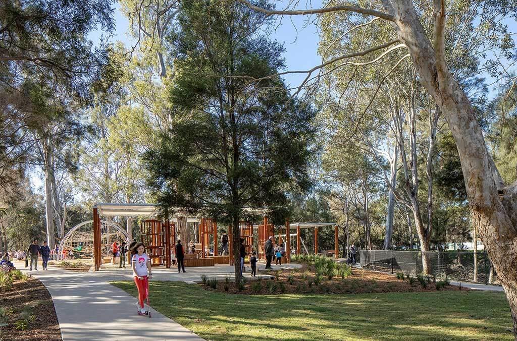 A lively park scene with people walking among trees and benches, enjoying nature and the fresh air together.