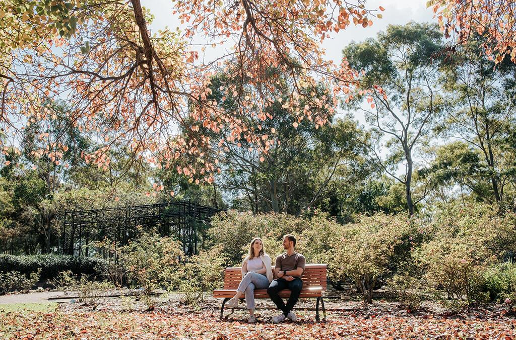 A man and woman sitting on a bench under a tree at Rumsey Rose garden.